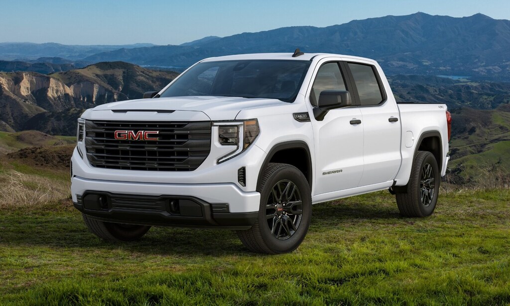 white GMC Sierra 1500 Denali on a grassy field backed by mountains